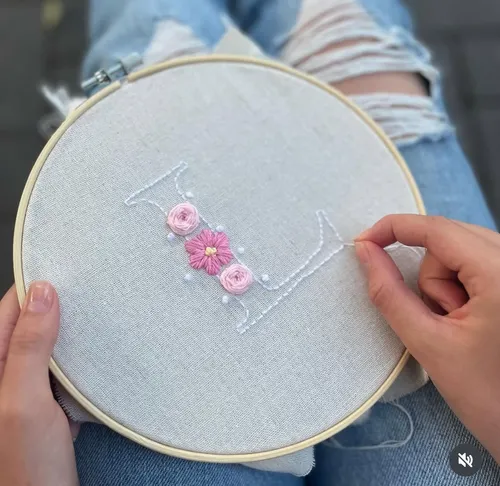 Hände sticken Blumendesign auf Stoffrahmen.