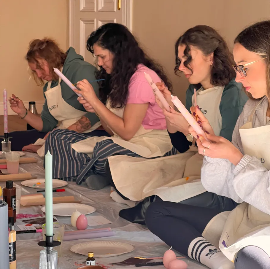 Four women sitting, painting candles, indoors.