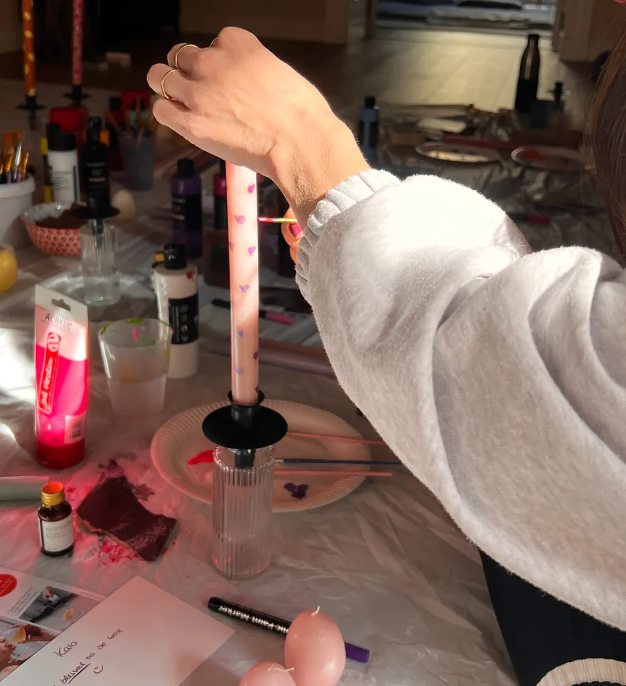 Person painting candle with hearts in crafting area.