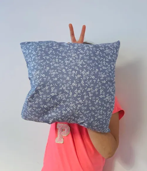 Person holding floral pillow, peace sign behind.