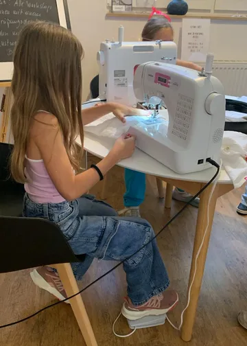 Girl using sewing machine at workshop.