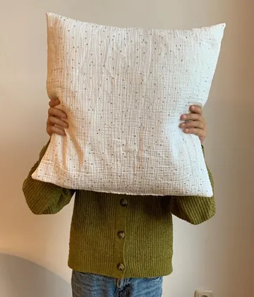 Person holding pillow covering face indoors.