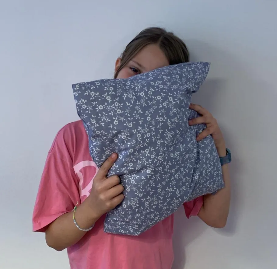 Person holding floral pillow against wall.