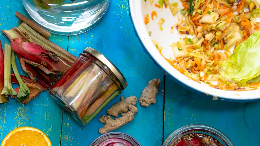 Assorted vegetables and jars on blue table.