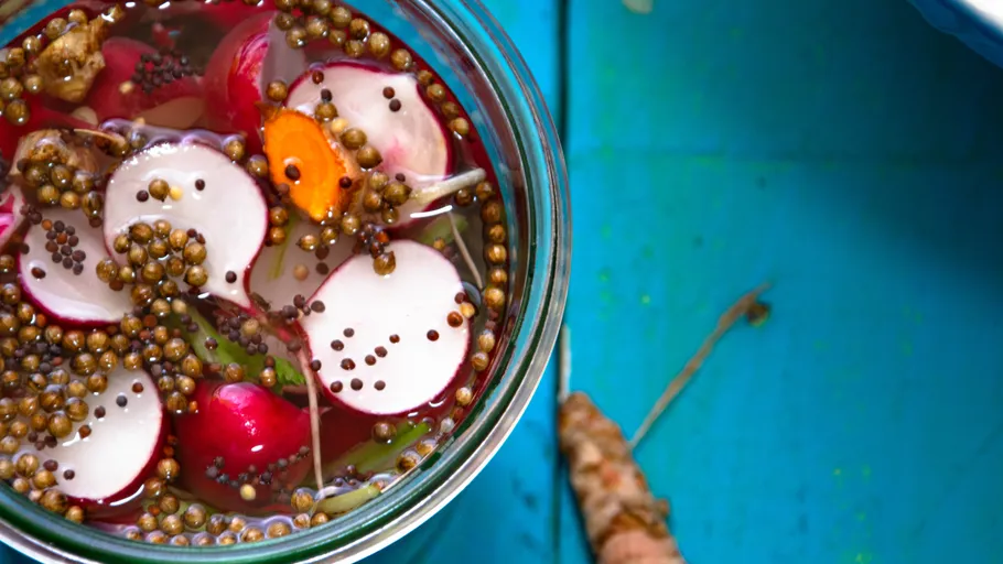 Pickled vegetables in a jar on blue surface.