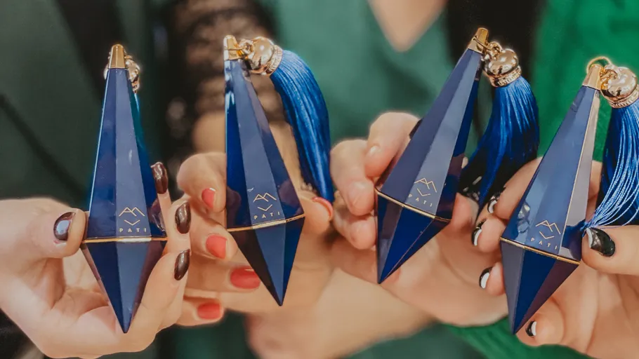 Hands holding blue perfume bottles with tassels.