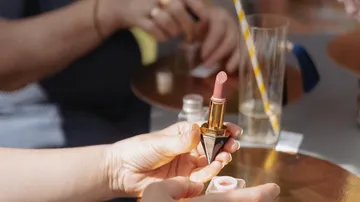 Hände halten Lippenstift auf goldenem Tablett.