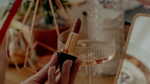 Hand holding lipstick near mirror and glass.