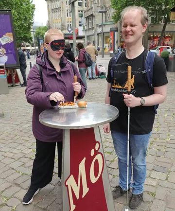 Zwei Personen an einem Stehtisch mit Stöcken.