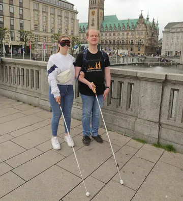 Zwei Personen mit Stöcken auf einer Brücke stehend.