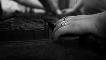 Hand mit Ringen berührt strukturierte Oberfläche.