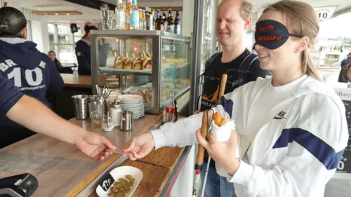 Blindfolded woman buying food at a counter.