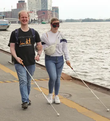 Zwei Personen mit Stöcken gehen am Wasser entlang.