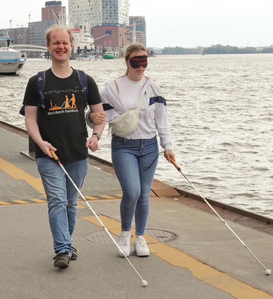 Two people with canes walking by waterfront.