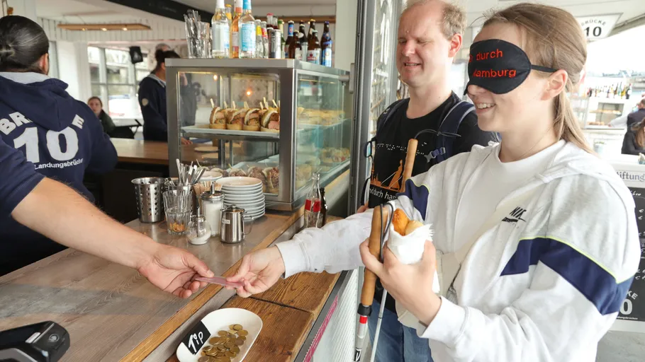 Blindfolded woman pays at a bakery counter.