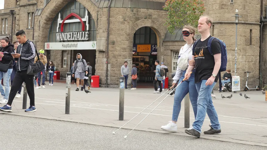 Blindfolded woman with cane walking with man.