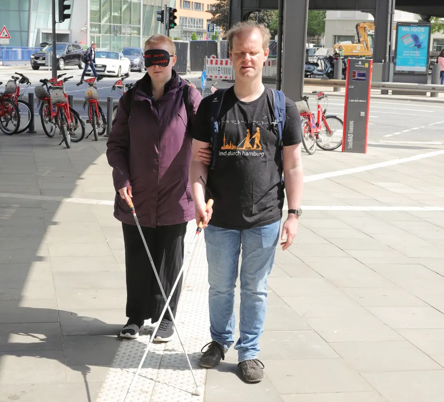 Two people with canes walking on city sidewalk.