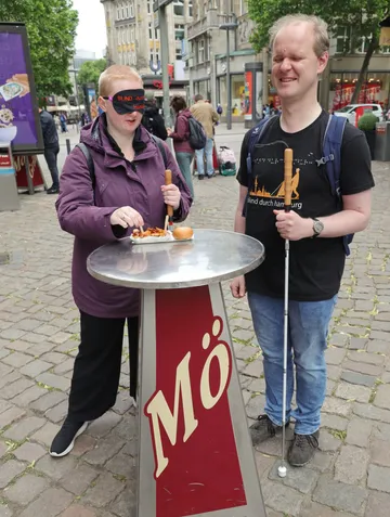 Zwei Personen essen an Stehtisch draußen.