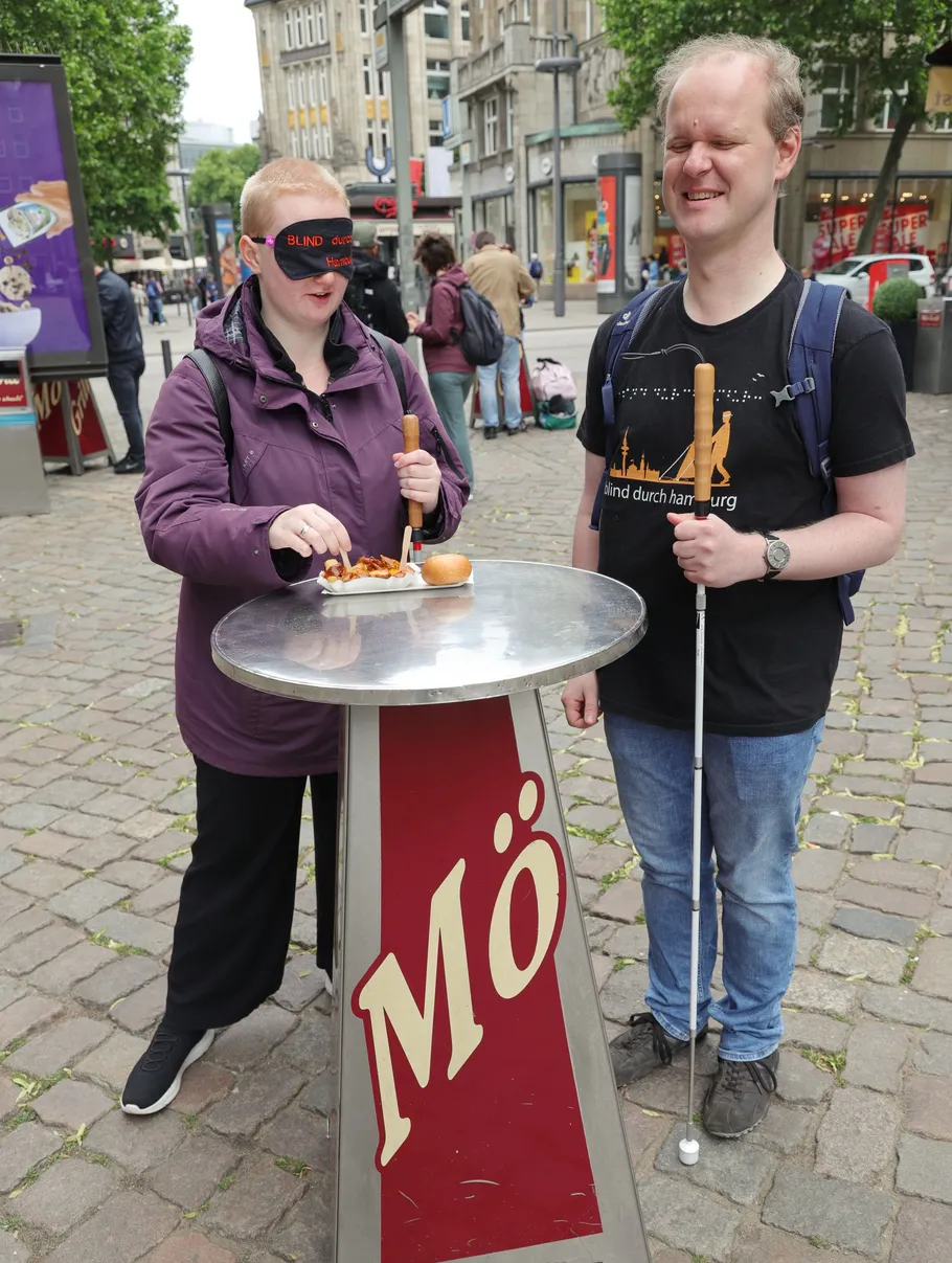 Two people eating at outdoor standing table.