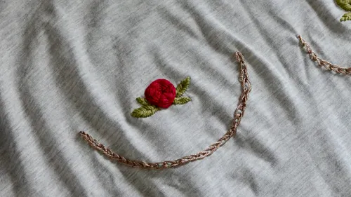 Rote Rosenstickerei auf grauem Stoff.
