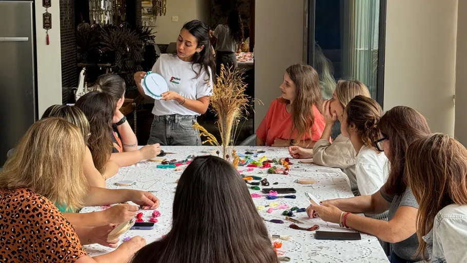 Woman demonstrating embroidery to seated group.