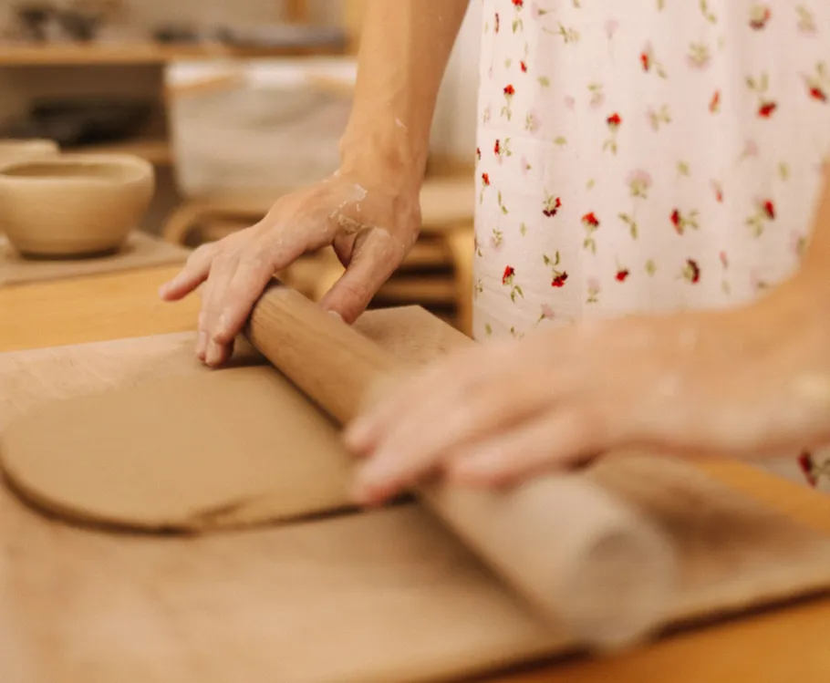 Hands rolling clay on wooden board.