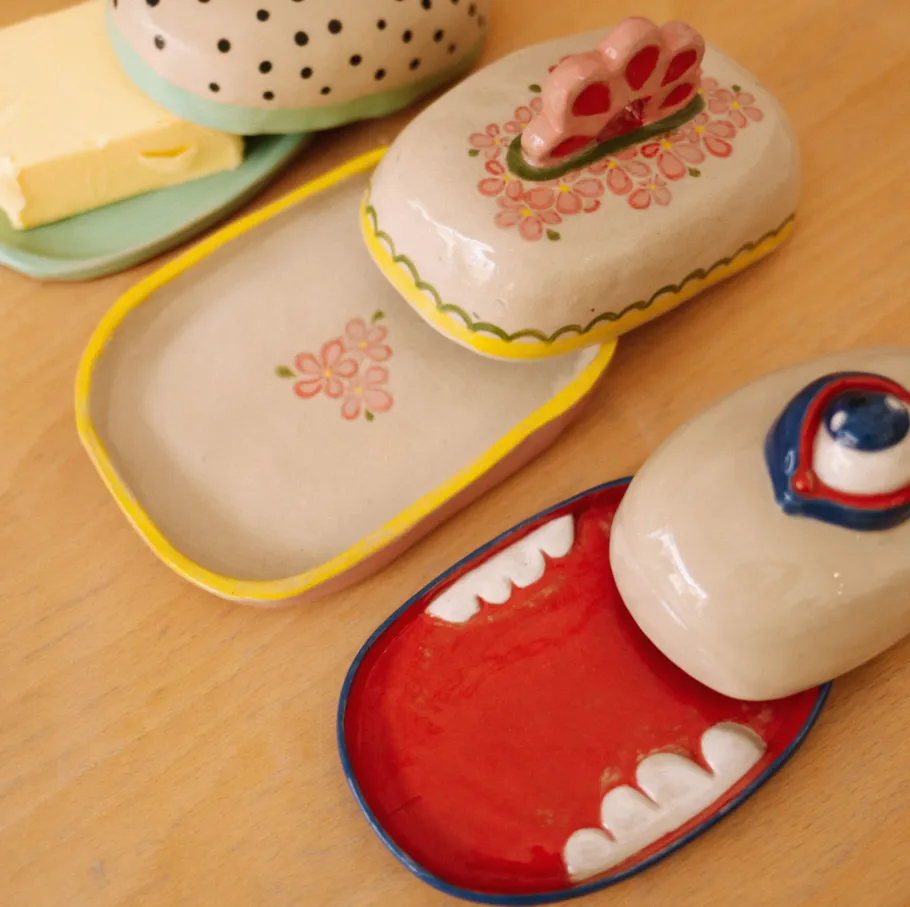 Bunte Keramik-Butterdosen auf einem Holztisch.