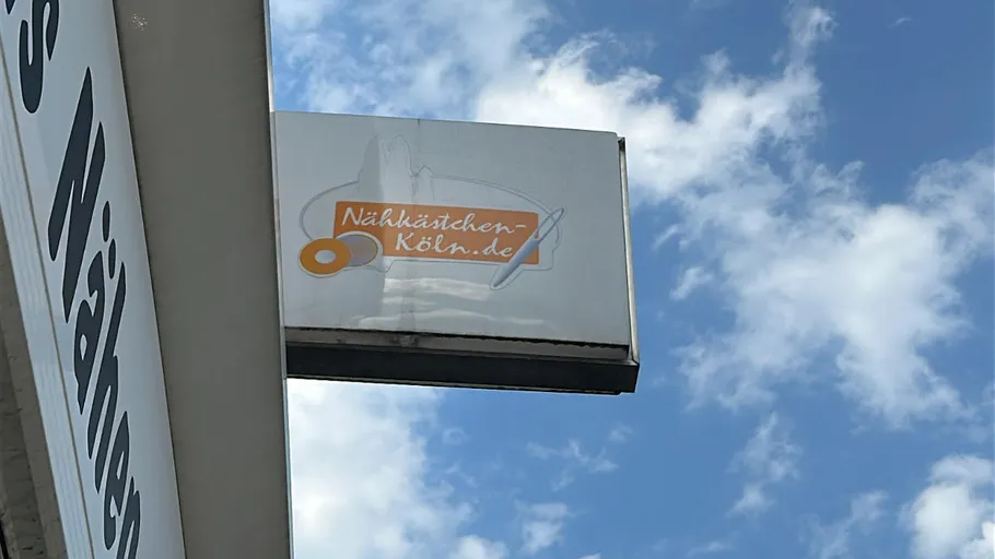 Shop sign with sewing logo against sky.