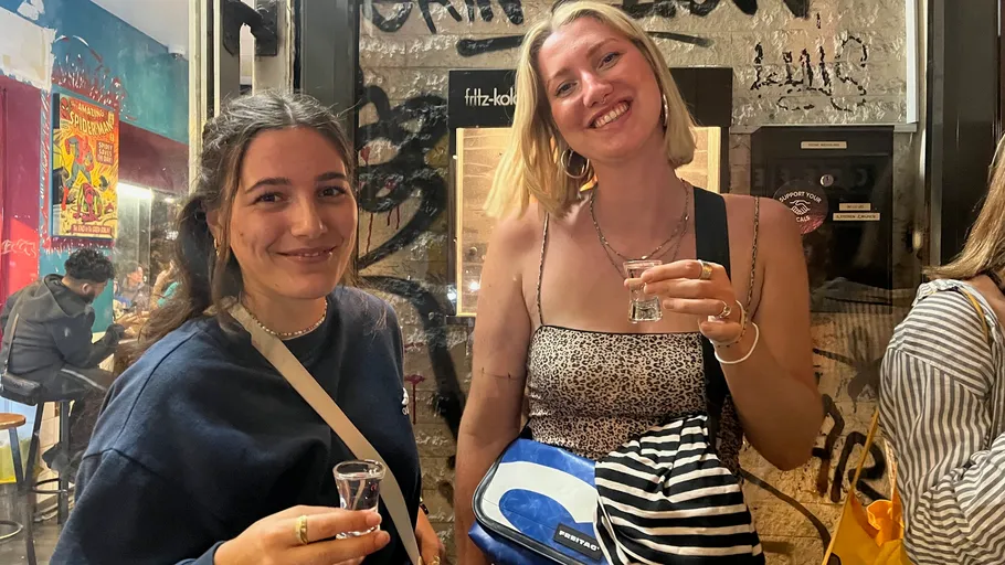 Two women smiling, holding drinks indoors.