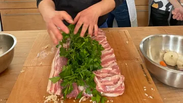 Person preparing meat with herbs, in kitchen.