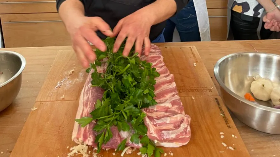 Person preparing meat with herbs, in kitchen.