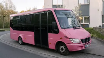 Pink bus parked on a street corner.
