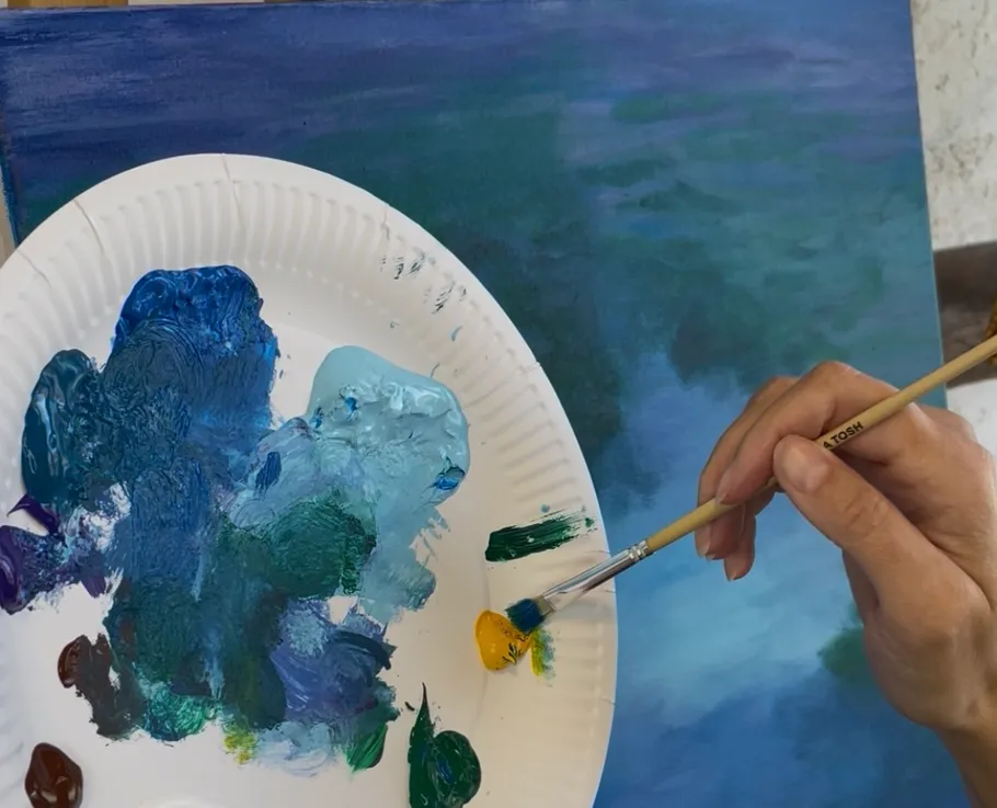 Artist mixing paint with brush on palette.