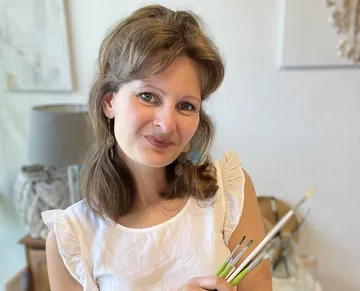 Woman holding paintbrushes, smiling indoors.