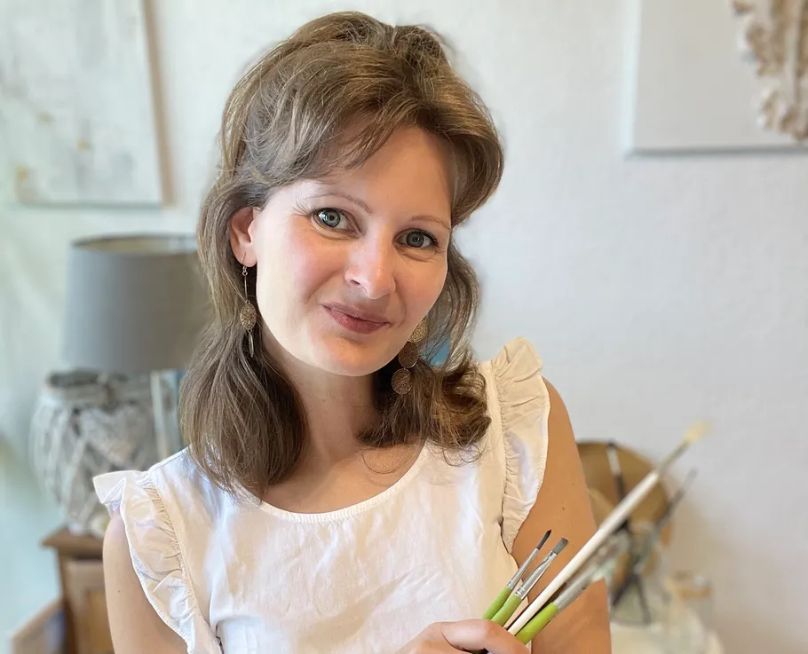 Woman holding paintbrushes, smiling indoors.