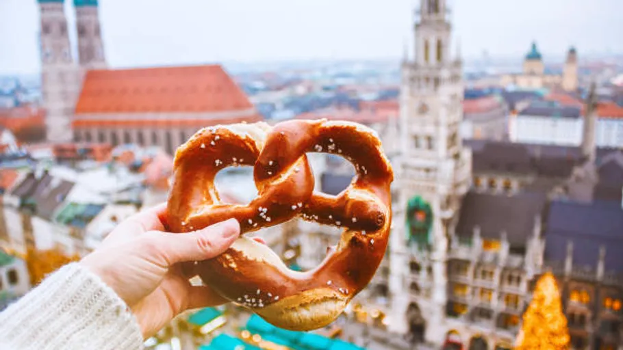 Hand hält Brezel über Stadtansicht mit Kirche.