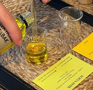 Hand pouring yellow liquid into small beaker.