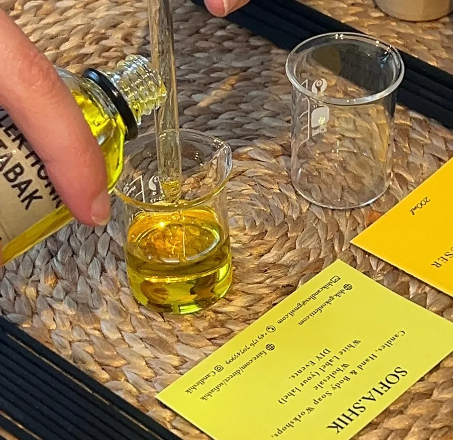 Hand pouring yellow liquid into small beaker.