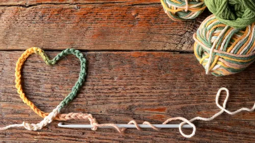 Heart-shaped yarn on wooden surface with knitting needles.