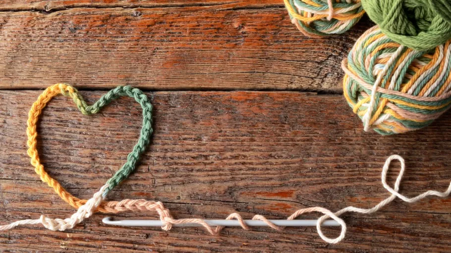 Herzförmiges Garn auf Holzoberfläche mit Stricknadeln.