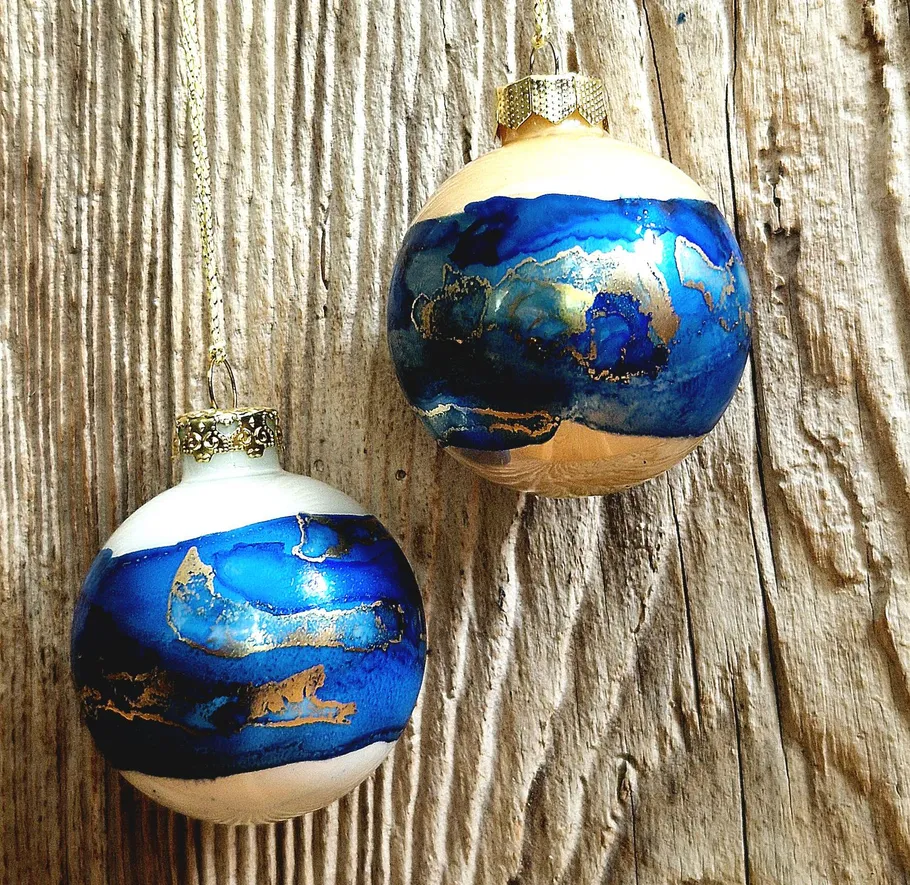 Zwei blaue und goldene Ornamente hängen auf Holz.