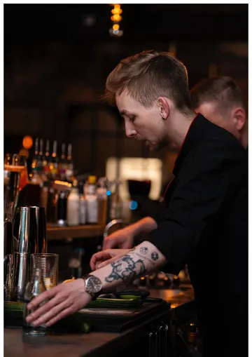 Tattooed bartender preparing drinks at a bar.