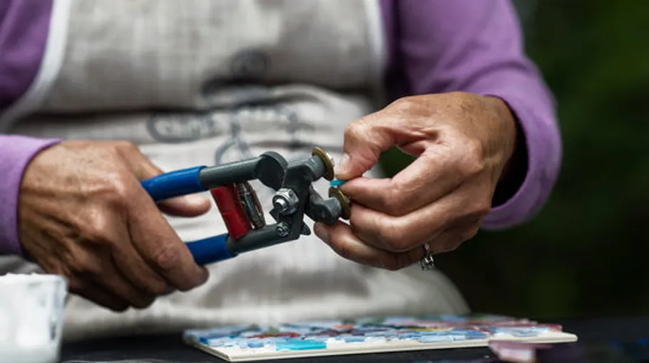 Hands using pliers on mosaic tiles.