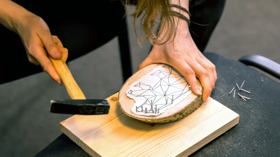 Person hammering nails on wood slab with design.