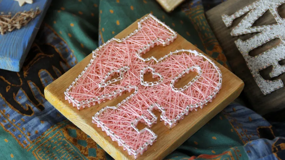 Wooden board with pink string heart design.