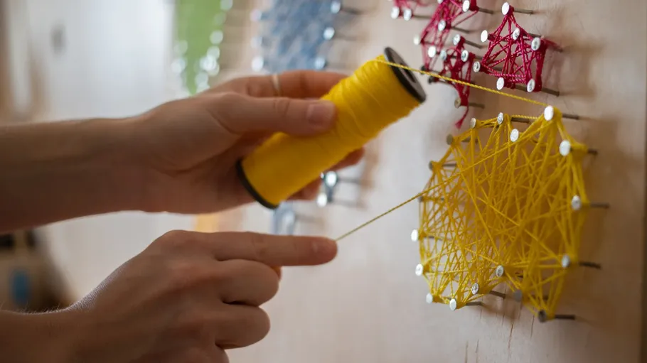 Hands stringing nails on a board.
