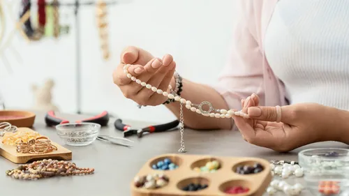 Person crafting jewelry at a cluttered workspace.