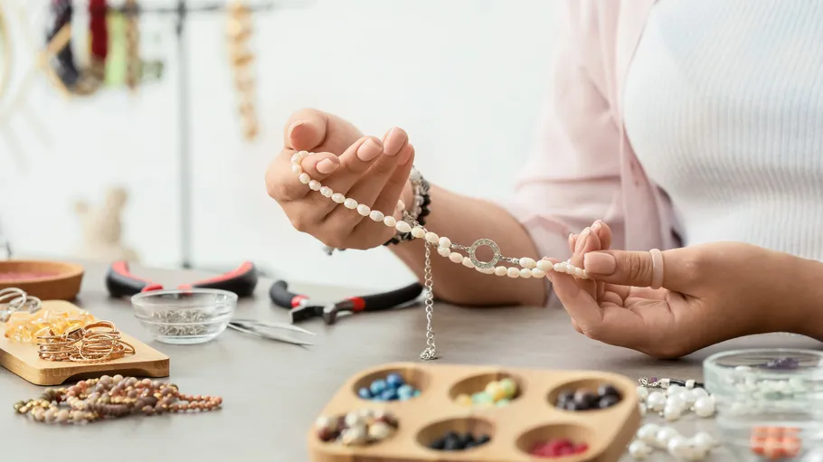 Person fertigt Schmuck an einem unordentlichen Arbeitsplatz.