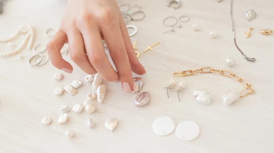 Hand arranging beads on a white surface.