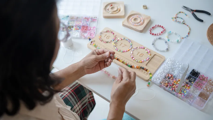 Person crafting beaded jewelry on a table.